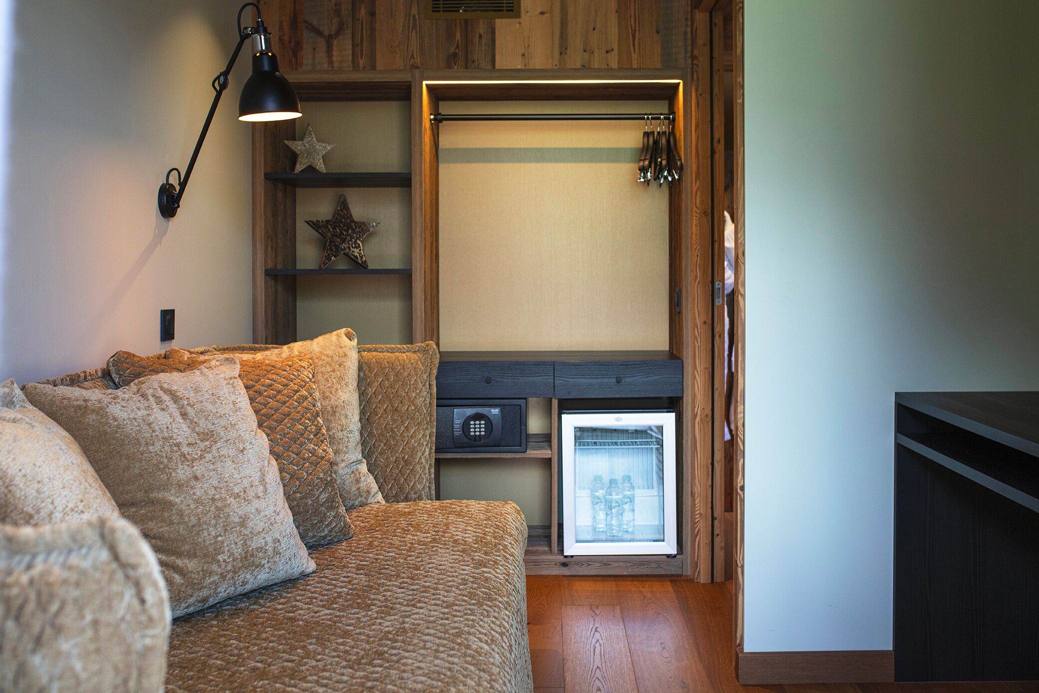 A cozy room with a wooden bench, a small refrigerator, and a wall-mounted shelf with decorative items.