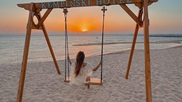 Eine Holz-Schaukel mit einem Schild, auf dem 'SOMABAY KEMPINSKI HOTEL' steht, an einem Strand bei Sonnenuntergang.