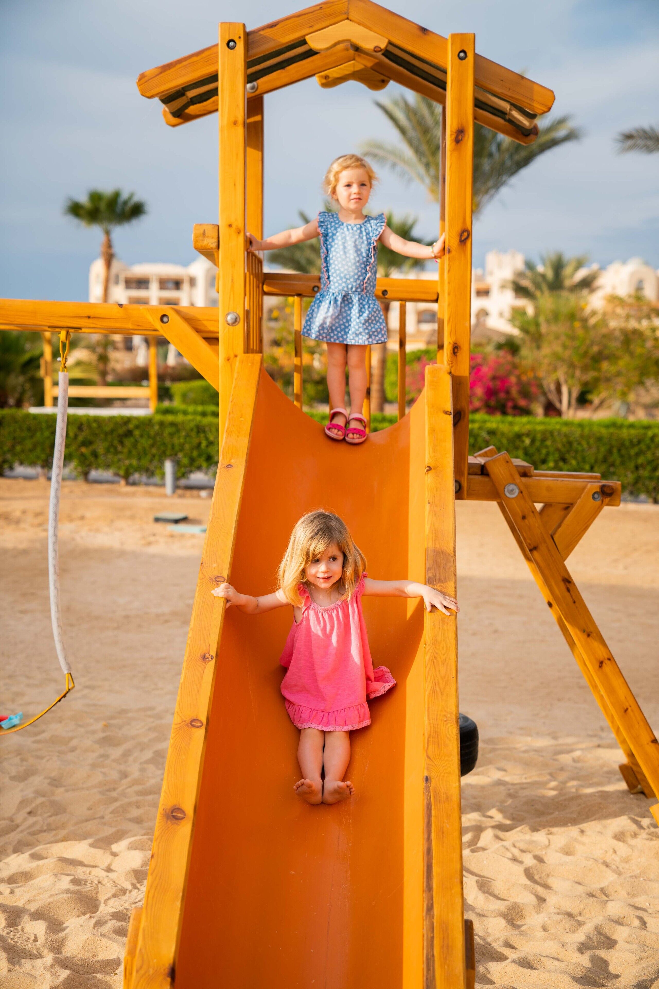 A wooden slide structure with two children at the top and bottom.