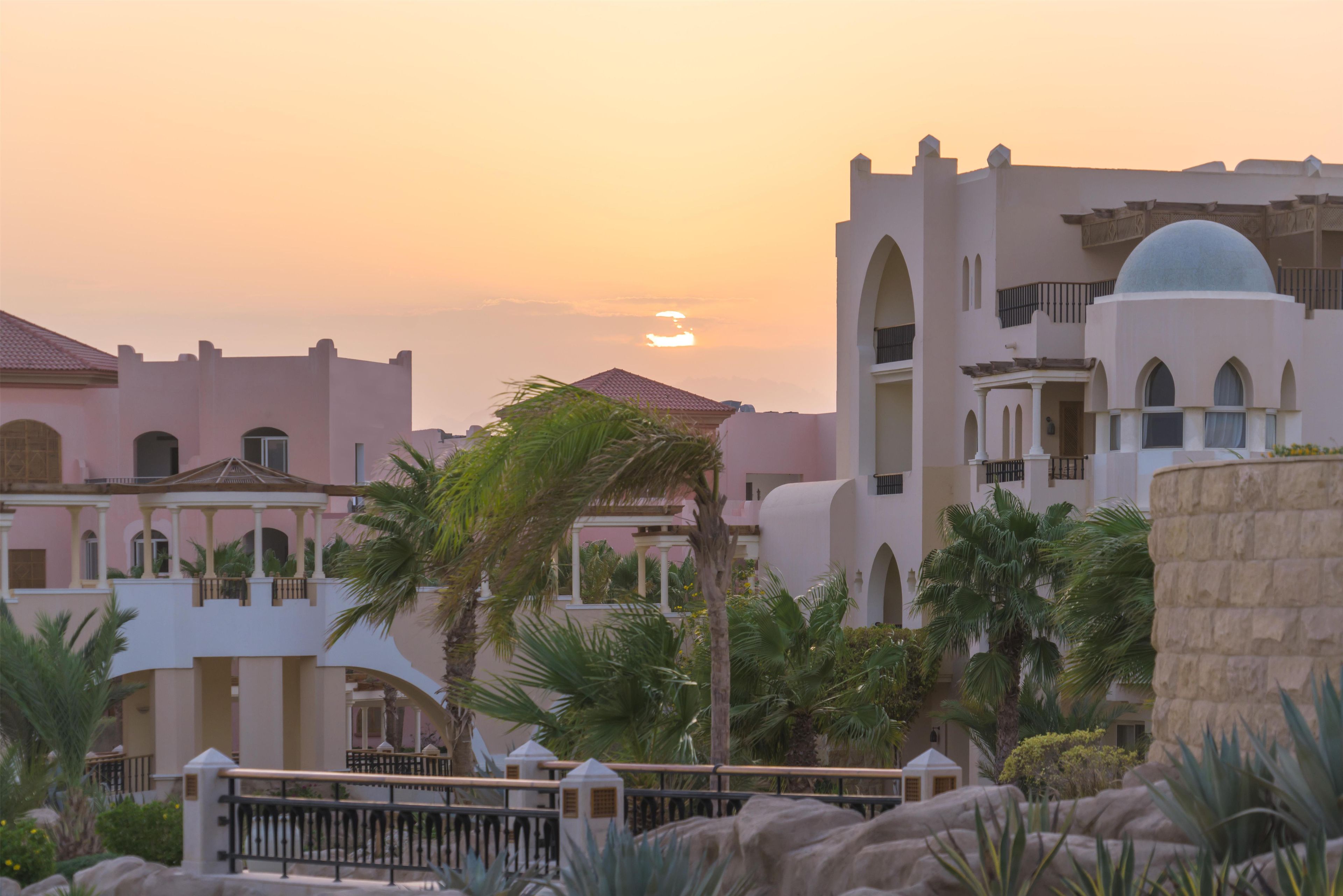 A resort with multiple buildings, palm trees, and a sunset.