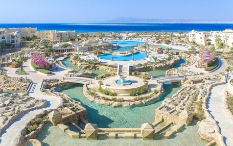 A resort with multiple swimming pools, a central fountain, and a view of the sea.