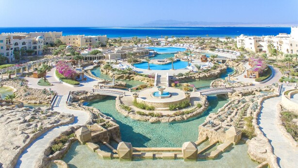 A resort with multiple swimming pools, a central fountain, and a view of the sea.