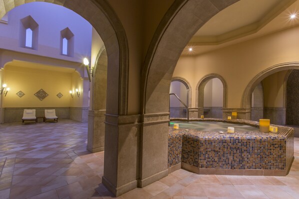 A spa area with a tiled hot tub, seating, and arches.