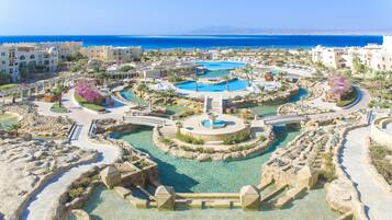 Un complejo turístico con varias piscinas, una fuente central y vistas al mar.