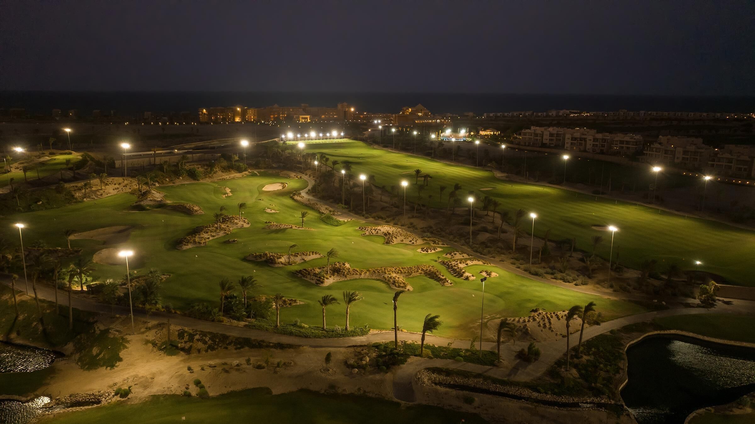 A golf course at night with well-lit paths and sand bunkers.