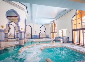 Une piscine intérieure luxueuse, dotée de plusieurs jacuzzis, et entourée d’arches décoratives et de murs recouverts de carreaux.
