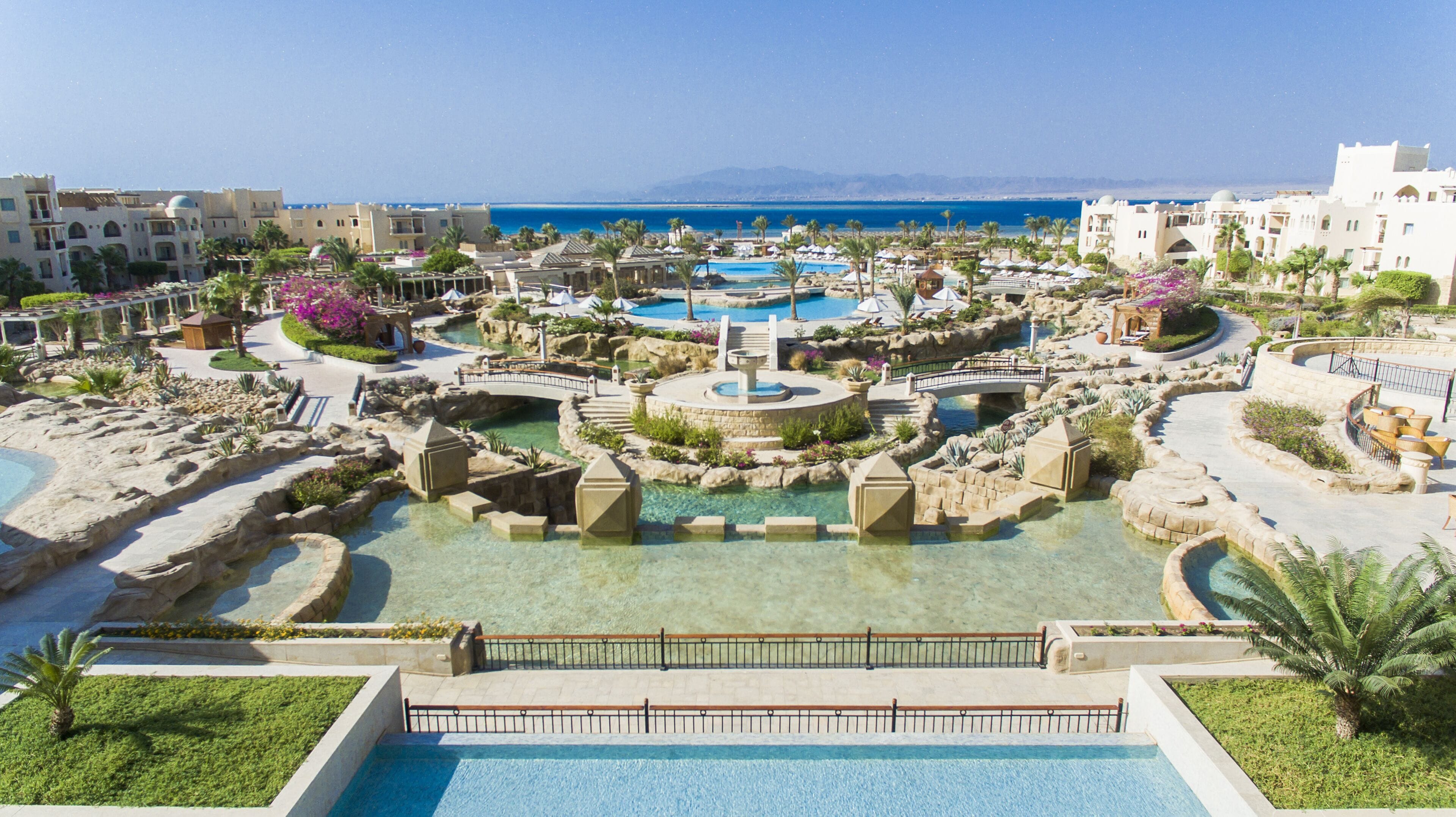 Ein Resort mit einem zentralen Pool, mehreren kleineren Pools und einer Brücke, die verschiedene Bereiche verbindet.