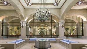 Un hall d’entrée spacieux avec un espace salon central, un lustre et des colonnes en arc de cercle.