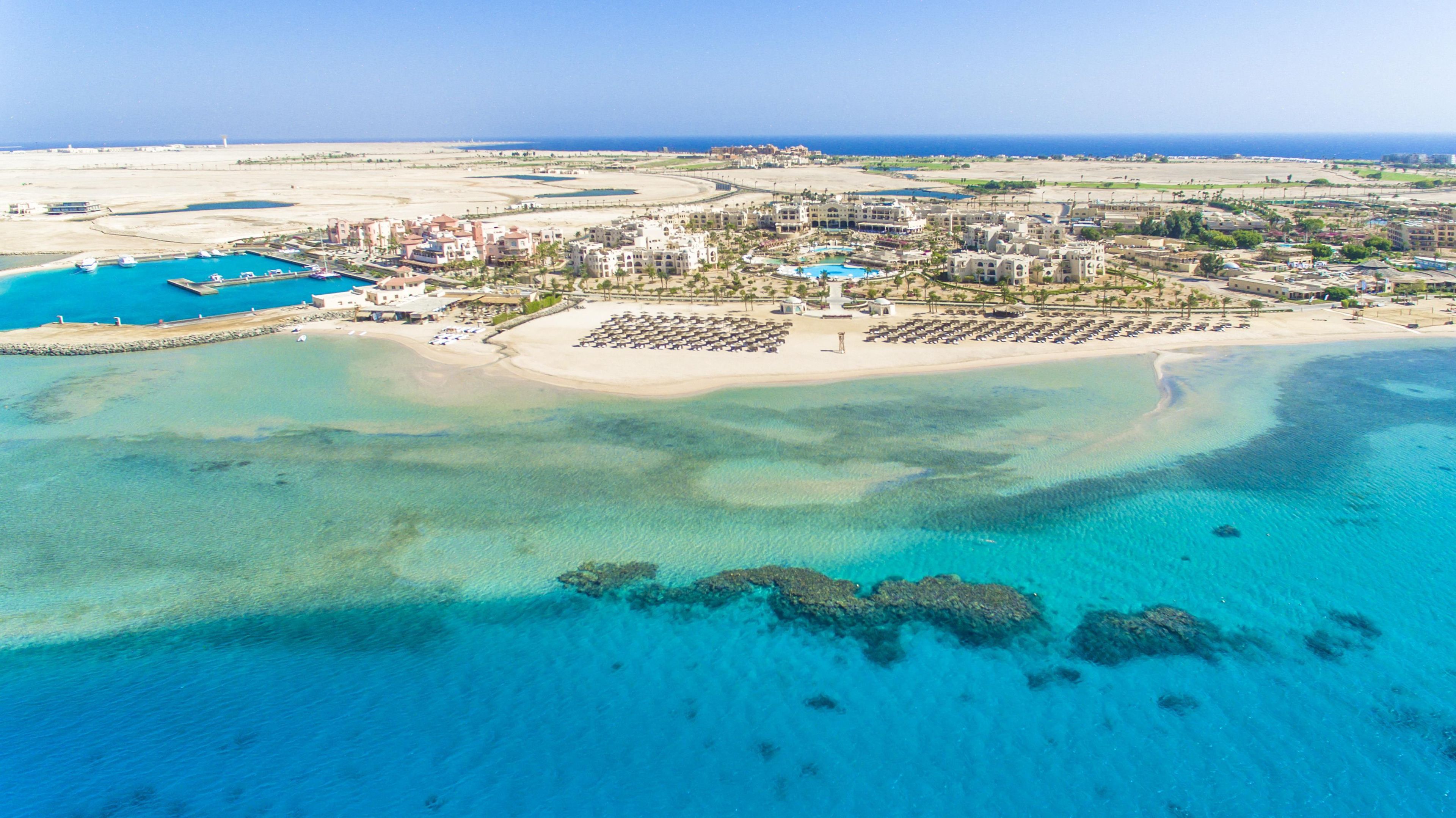 Luftaufnahme eines Küstenresorts mit mehreren Gebäuden, einer Marina und einem Strand.