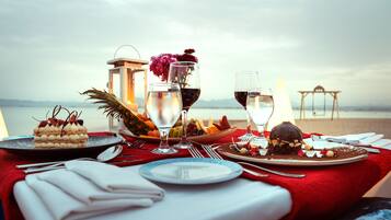 A table set for a meal with a view of the sea, including plates, glasses, and a lantern.