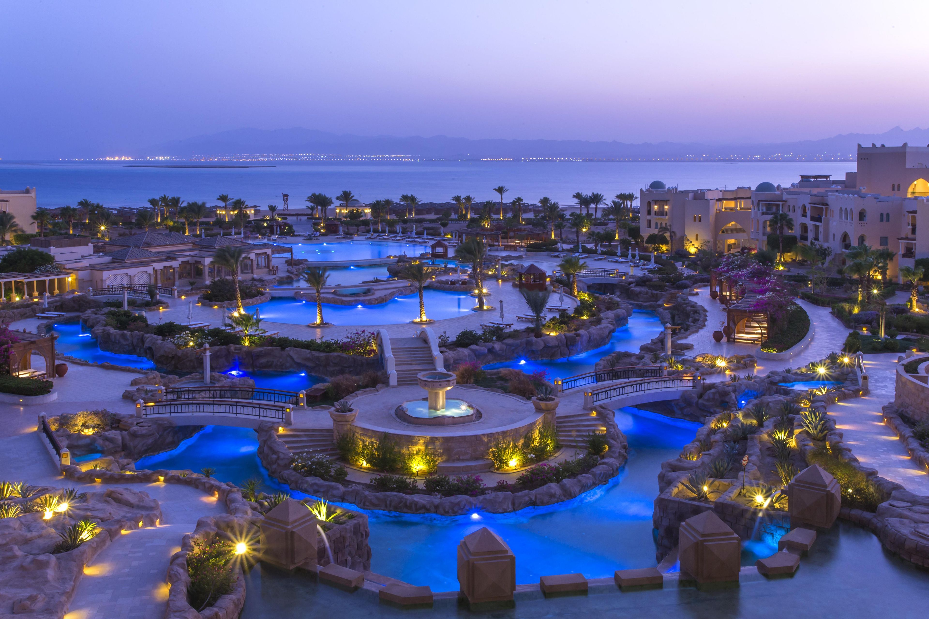 Un resort con varias piscinas, palmeras y vistas al mar.