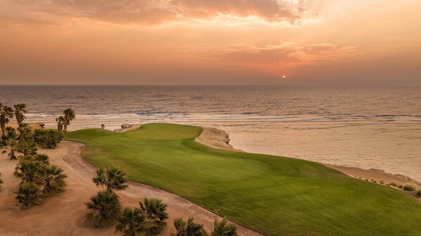 Um campo de golfe com vista para o oceano ao pôr do sol.