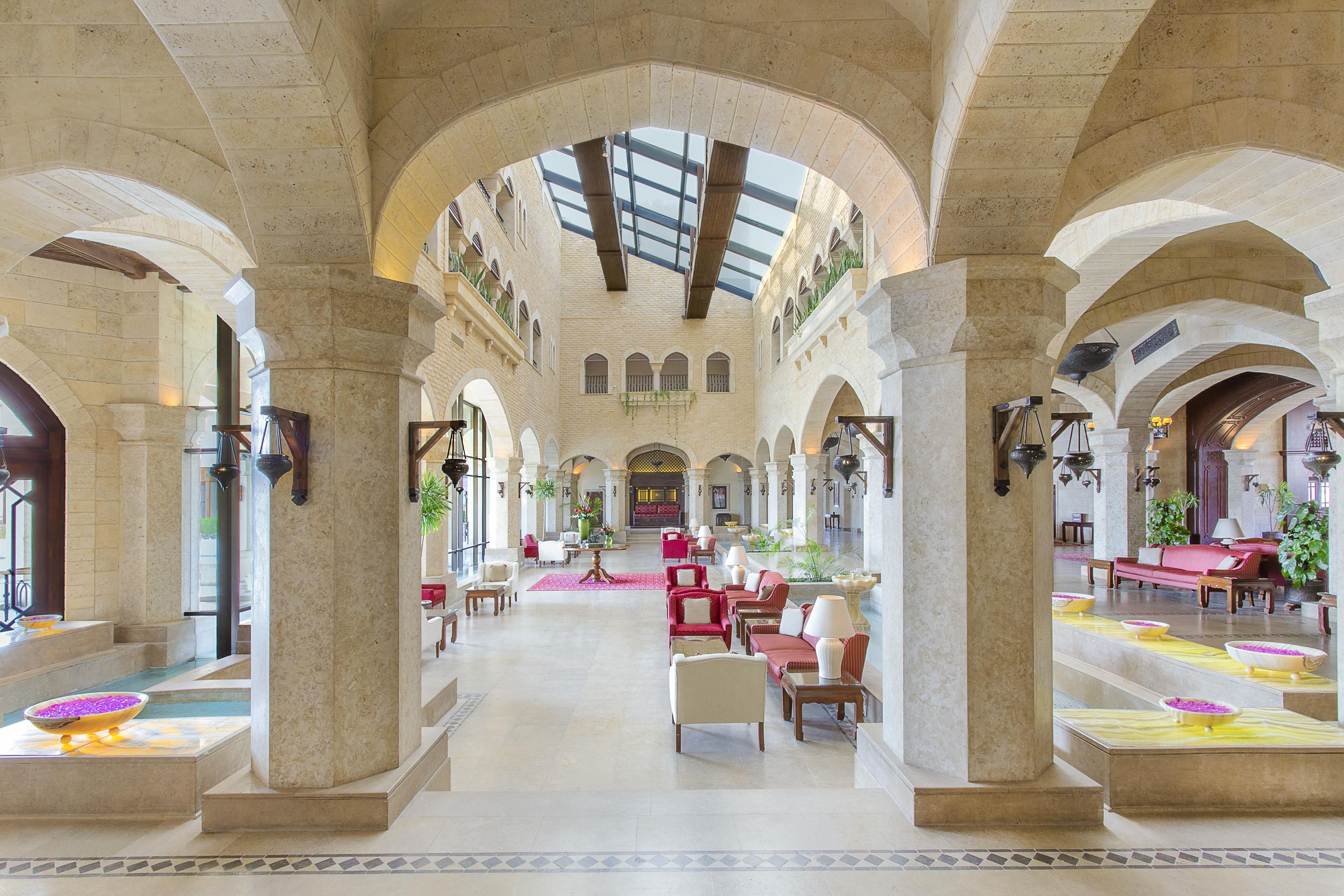 A spacious lobby with high ceilings, arched columns, and a central seating area with red sofas.