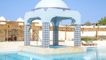 A pool area with a tiled gazebo structure, lounge chairs, and a clear blue sky.