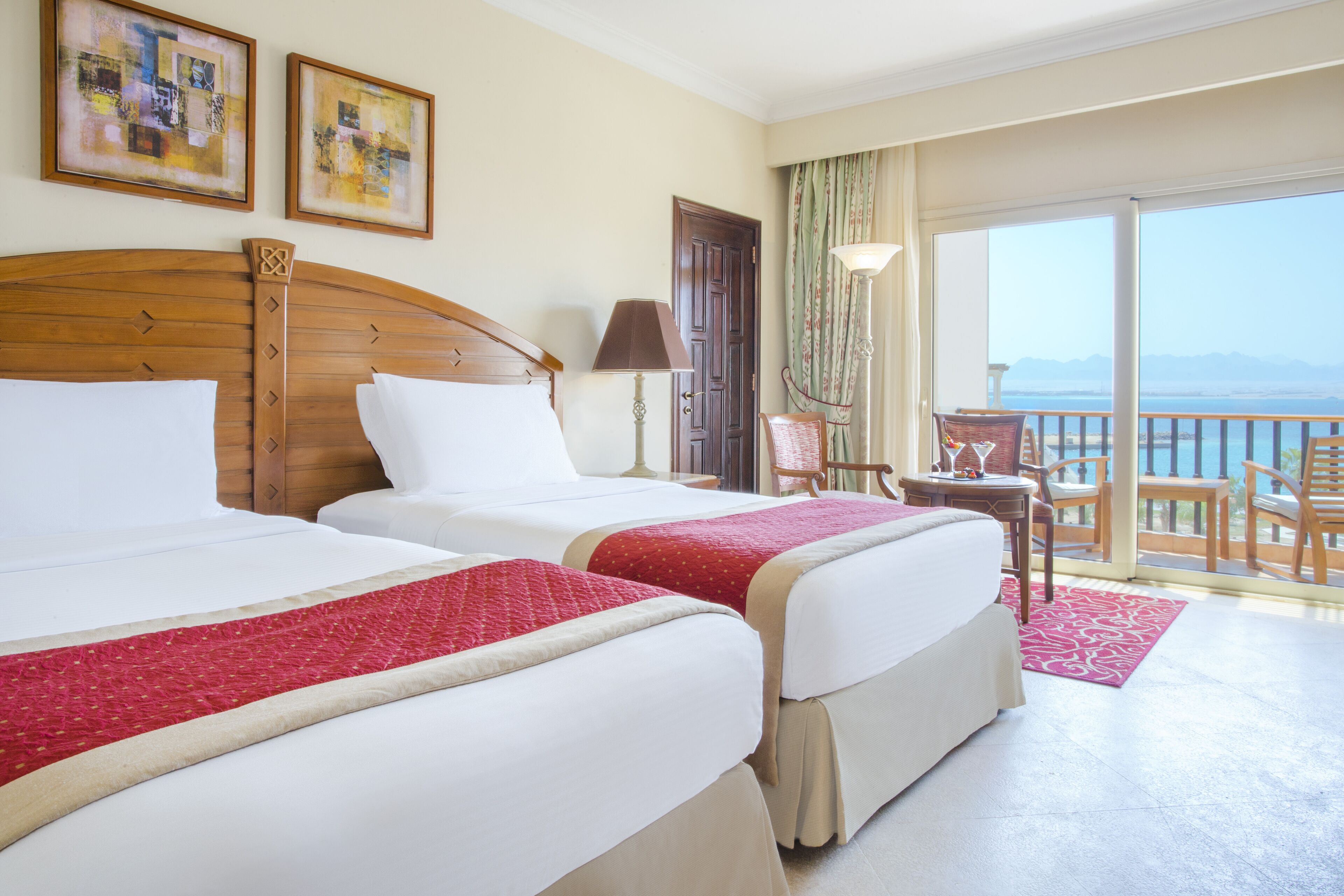 A hotel room with two beds, a balcony with a view, and a desk with a chair.
