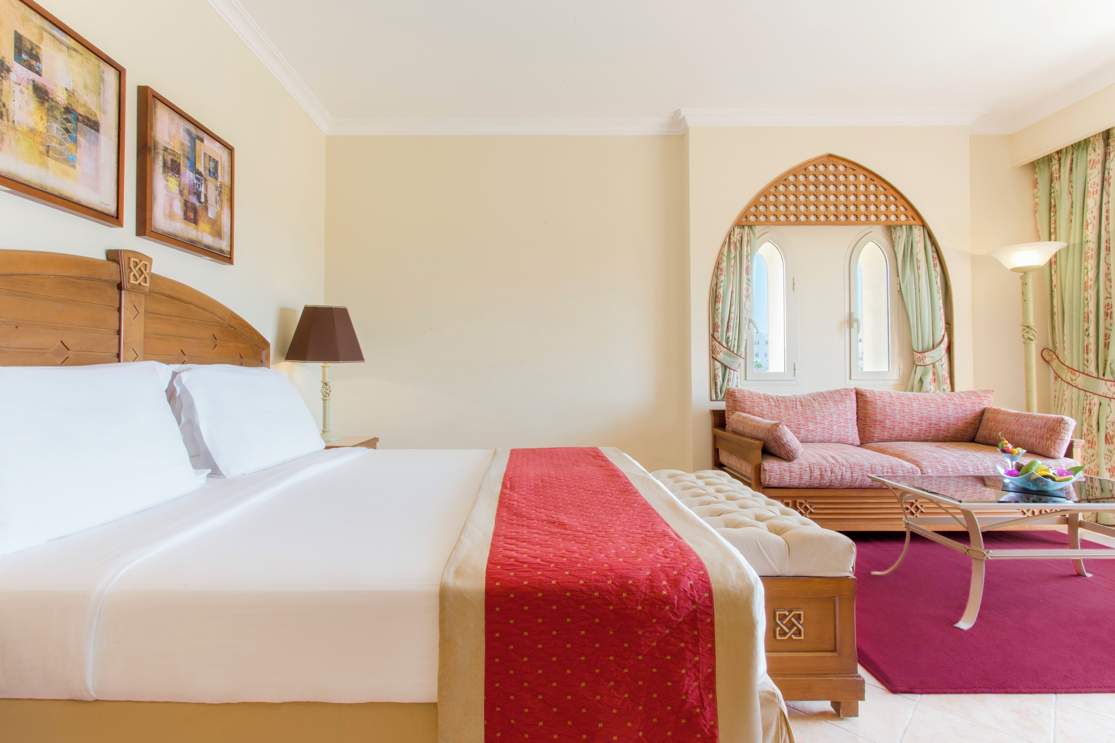 A hotel room with a large bed, a sofa, a small table, and a mirror.