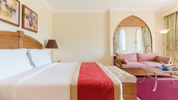 A hotel room with a large bed, a sofa, a small table, and a mirror.