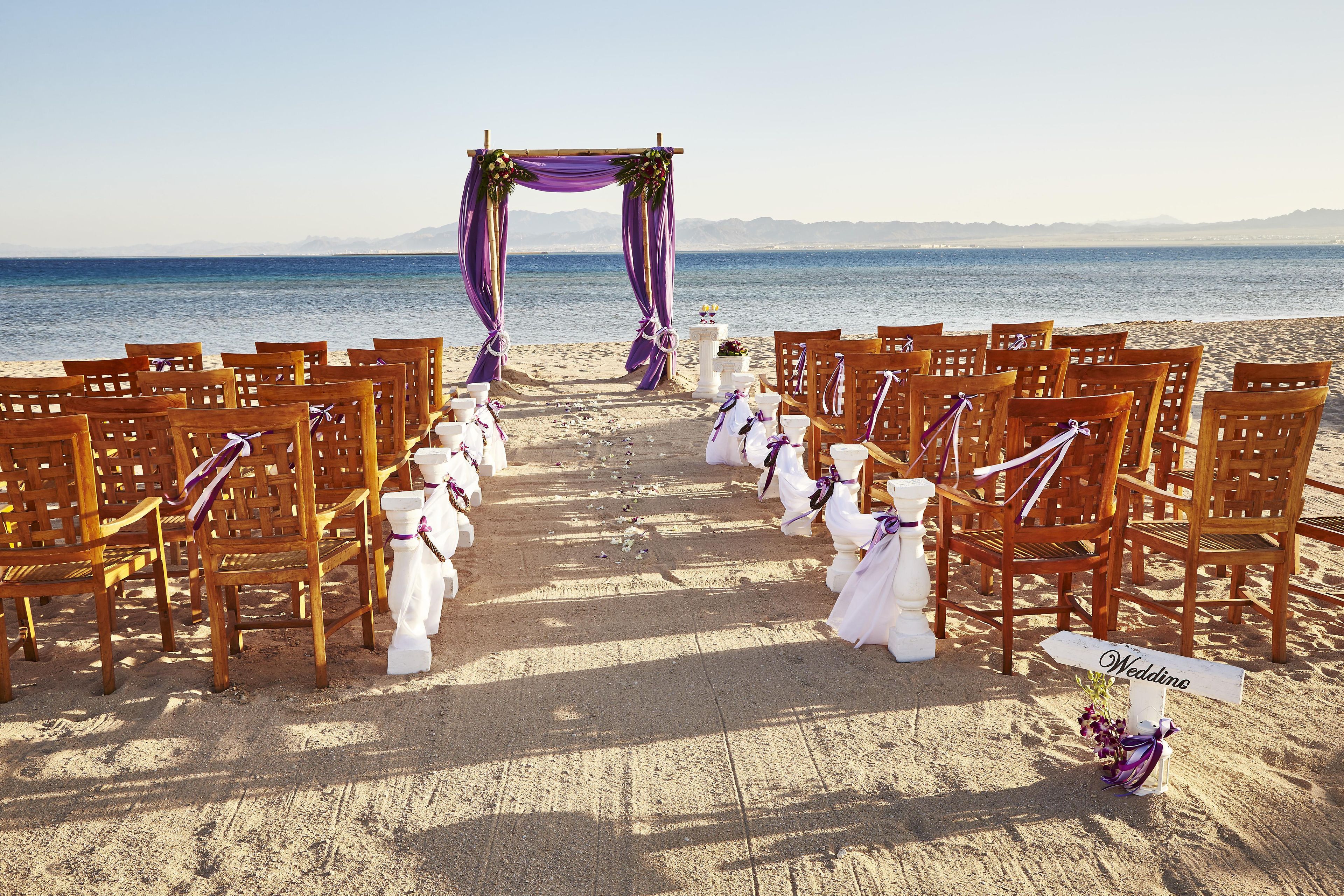 A beach wedding setup with wooden chairs and a white aisle.