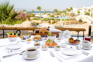 Una mesa preparada con alimentos para el desayuno y vista a una piscina y edificios de un resort.
