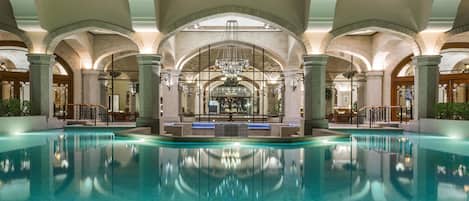 A large indoor swimming pool with arched ceilings and a central chandelier.