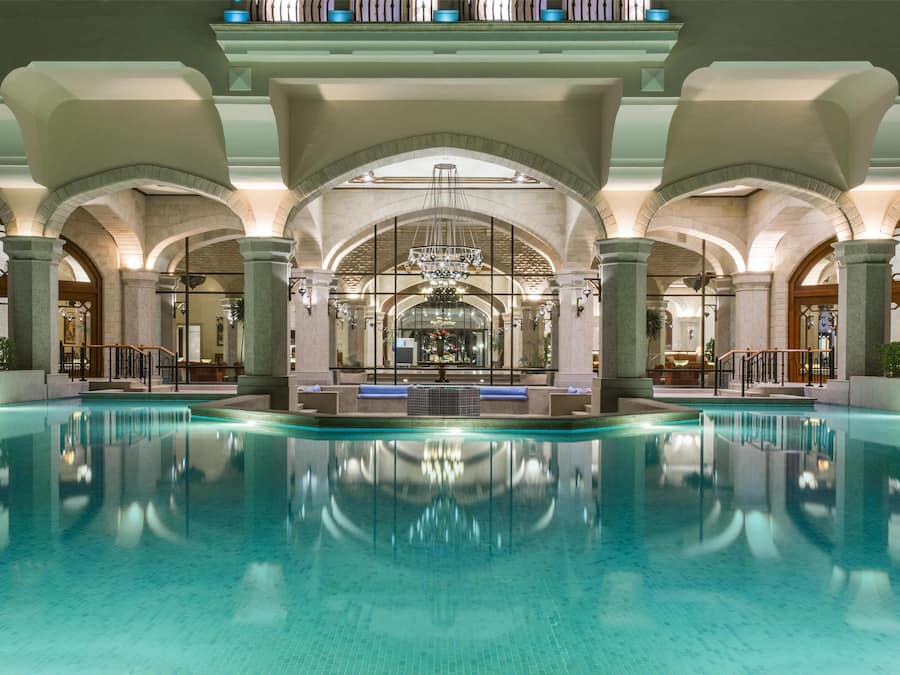 Una amplia piscina interior con techos abovedados y un candelabro central.