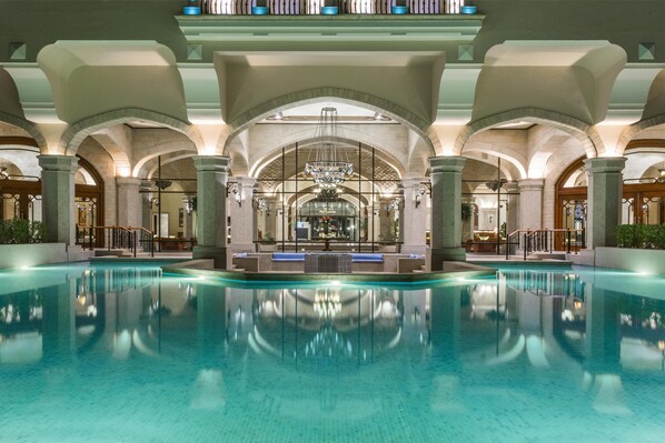Una amplia piscina interior con techos abovedados y un candelabro central.