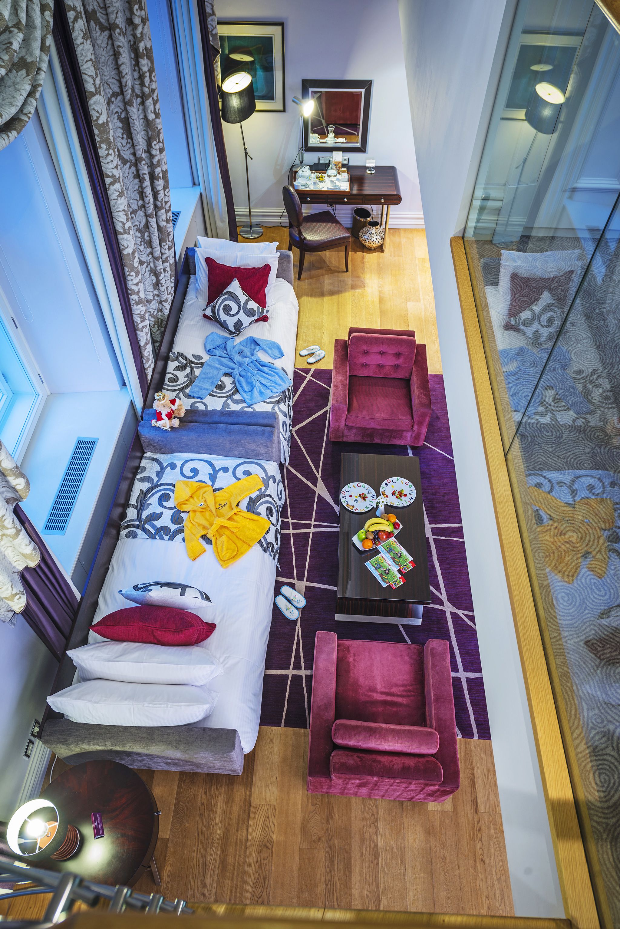 Quarto de hotel moderno com sofá, duas poltronas, uma mesa de jantar e um separador de vidro.