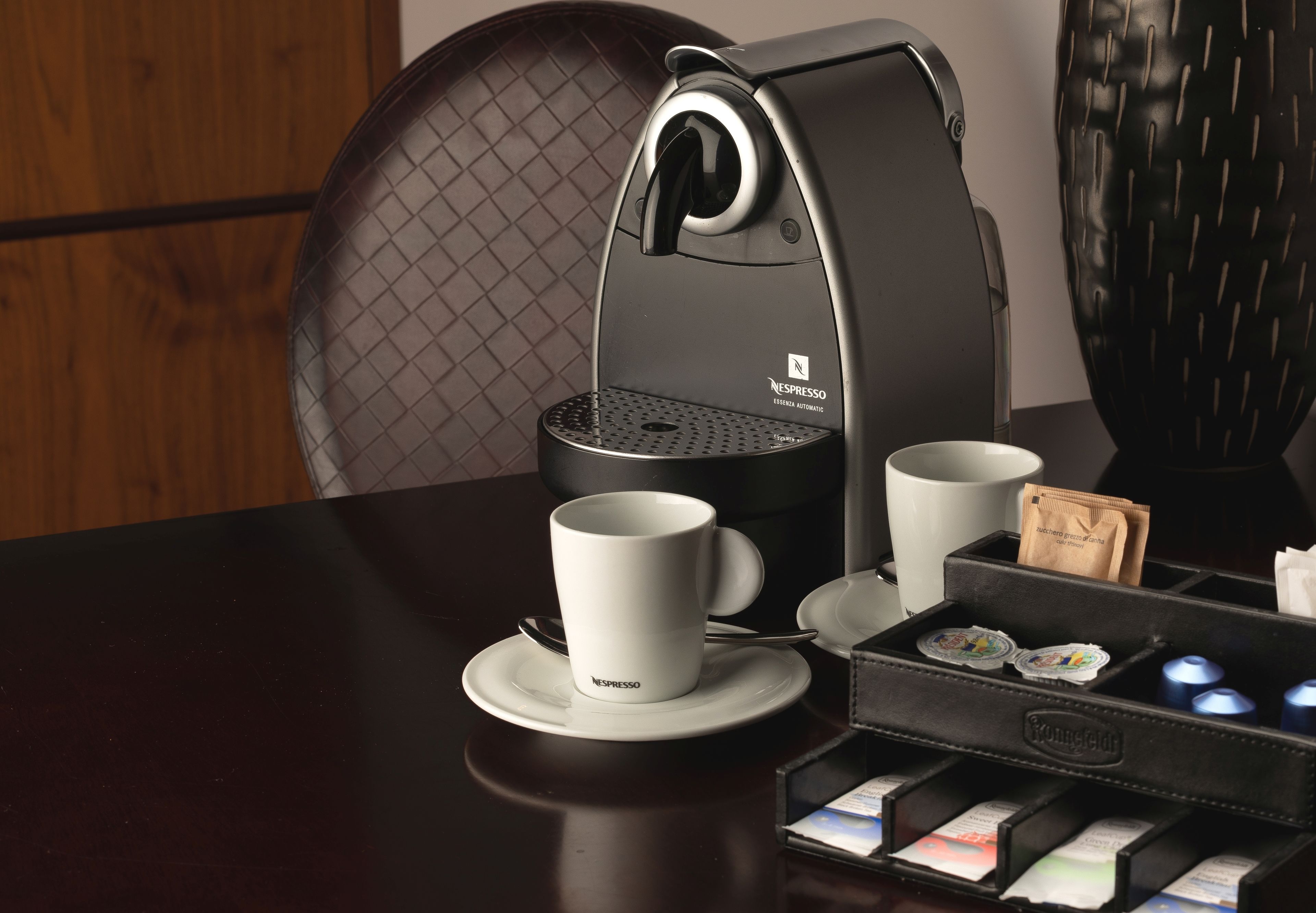 Eine Nespresso-Kaffeemaschine mit Tasse und Untertasse, einem Podhalter und einer kleinen Ablage für Kaffeekapseln.