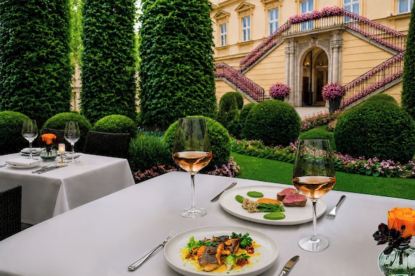An outdoor dining area with tables set for two, each with a glass of wine, plates of food, and cutlery.