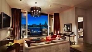 A modern hotel room with a large window offering a city view, a comfortable seating area, a flat-screen TV, and a desk with a laptop. - The Grand Mark Prague - The Leading Hotels of the World (Prague)