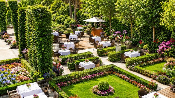 An outdoor garden with tables and chairs, surrounded by lush greenery and flowers. - The Grand Mark Prague - The Leading Hotels of the World (Prague)