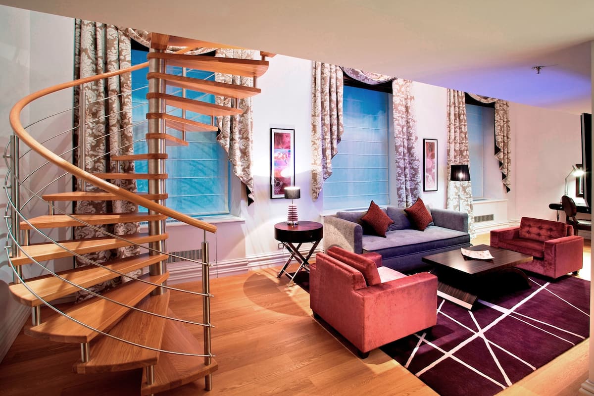 A modern living room with a spiral staircase, a blue window, a sofa, and a red armchair.