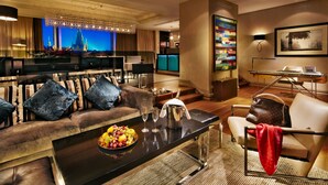 A modern living room with a sofa, armchairs, a coffee table with fruit and glasses, a TV, and a cityscape view. - The Grand Mark Prague - The Leading Hotels of the World (Prague)