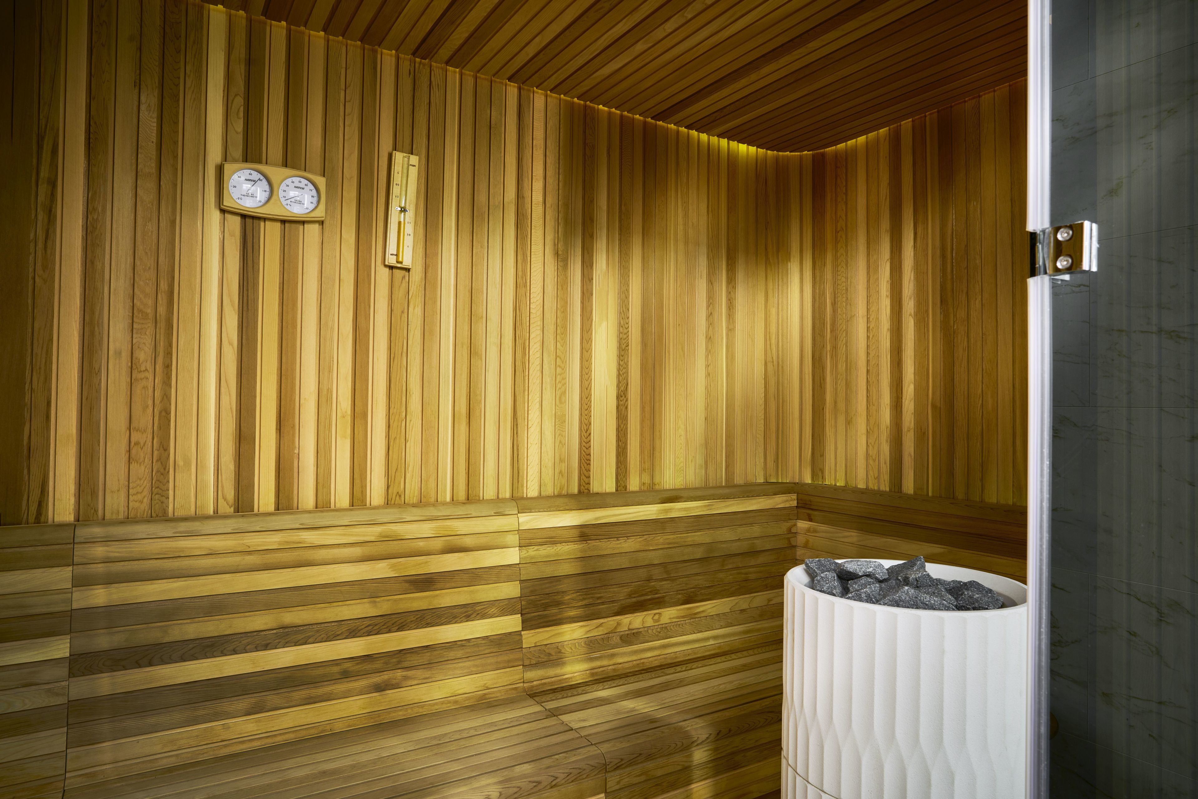 A sauna with wooden walls and benches, a clock, and a trash bin.