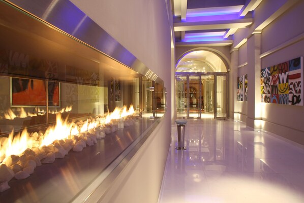A modern hotel corridor with a glass fireplace, art on the walls, and a polished floor.