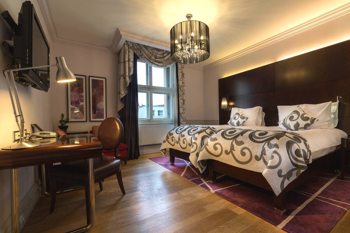 A hotel room with a bed, desk, chair, and a large window with curtains.