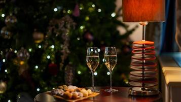 A table with two glasses of white wine, a plate of pastries, and a lamp with a red base.