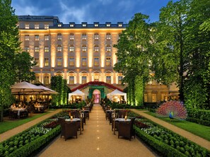 Et hotel med en elegant indgang, udendørs spiseområde og velplejede haver.