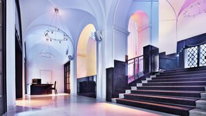 A grand lobby with high ceilings, arched doorways, and a staircase leading to upper floors. - The Grand Mark Prague - The Leading Hotels of the World (Prague)