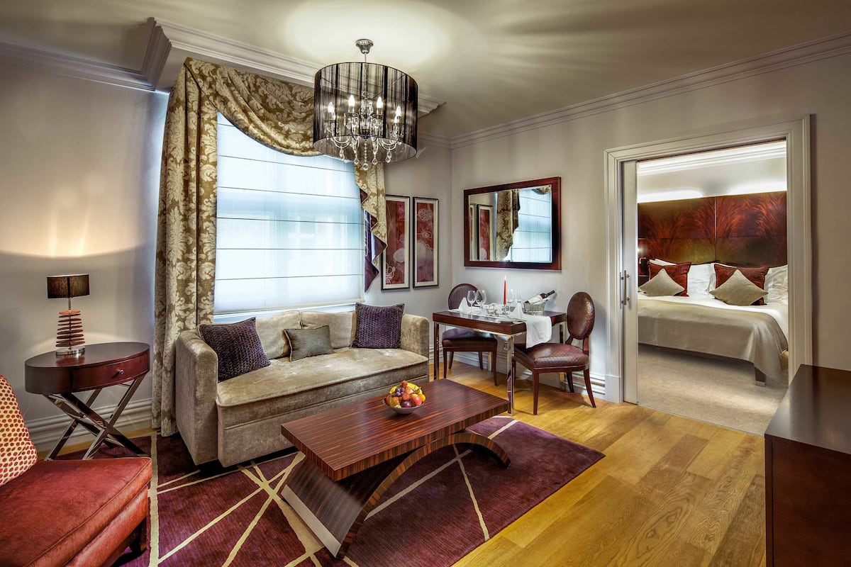 A well-lit room with a sofa, a dining table, a chandelier, and a bed with a headboard.