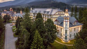 A large, multi-story hotel with a central tower, surrounded by lush greenery and mountains in the background.