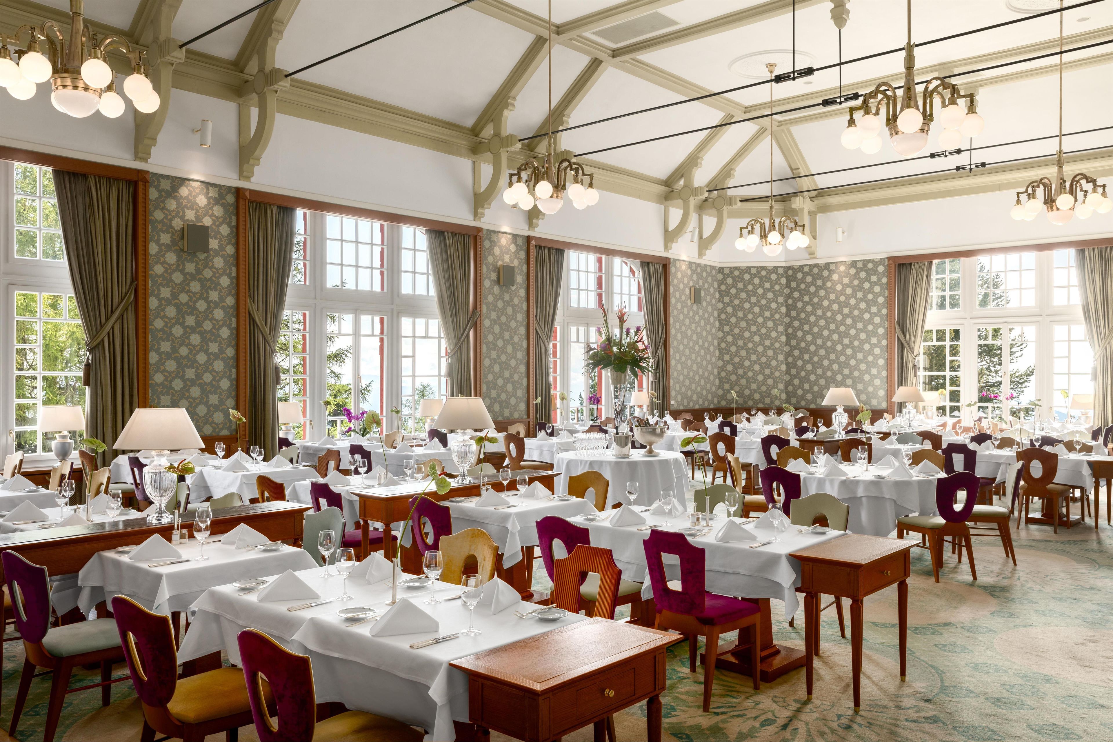 A formal dining room with multiple tables set for service, large windows, and classic chandeliers.