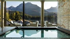 A pool area with two white sofas and a glass barrier, offering a view of a mountainous landscape.