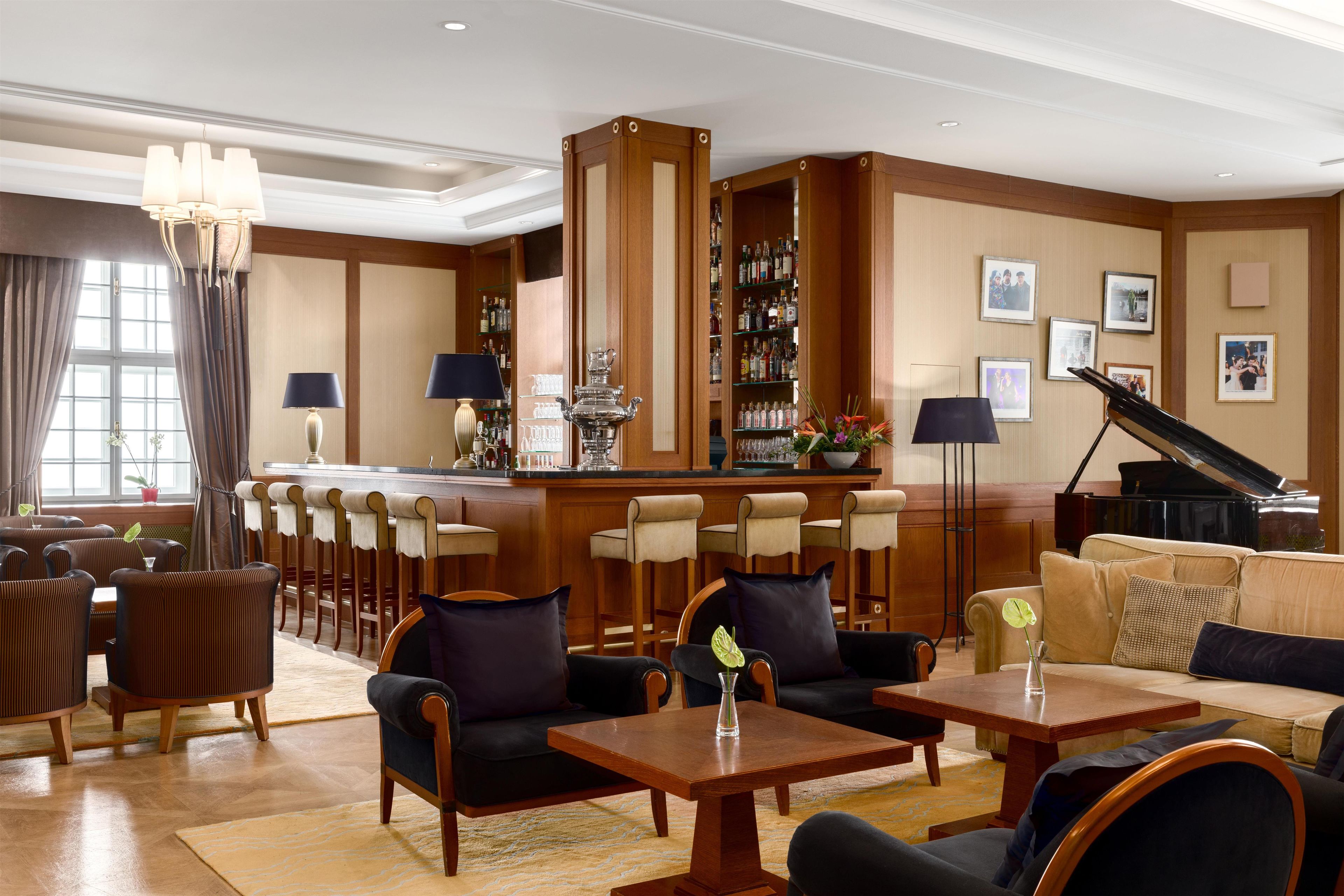 Un hall d’hôtel comprenant un bar, des espaces aménagés avec des sièges et un piano.