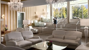 A spacious lobby with a large chandelier, comfortable seating, and a view of outdoor stairs and greenery. - Grand Hotel Kempinski High Tatras (Štrba)