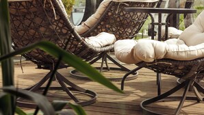 Wicker lounge chairs with cushions on a wooden deck, overlooking a body of water.