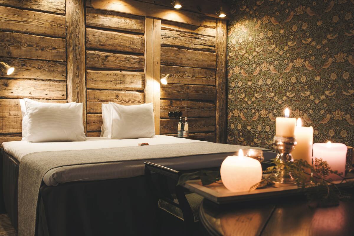 A wooden cabin-style room with a bed, candles, and a tray with flowers.