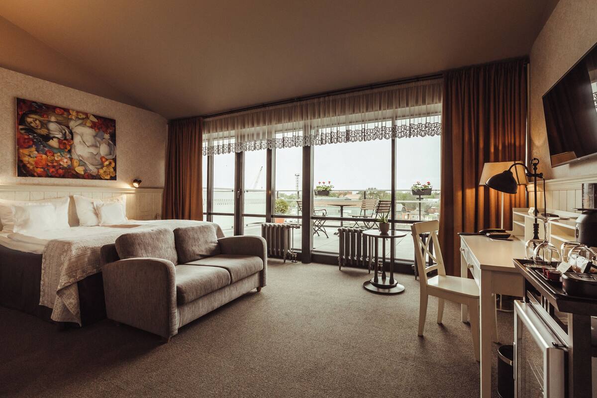 A hotel room with a bed, a sofa, a desk, a chair, and a television.