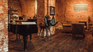 A room with exposed brick walls, wooden beams, a grand piano, and leather chairs.