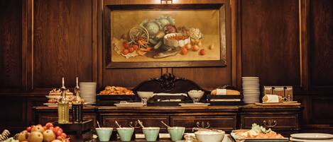 A buffet table with various food items and dishes, set against a backdrop of wooden paneling and a large painting.